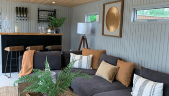 Stylish garden room bar with a dark corner sofa, warm cushions, bar stools and drinks shelving.